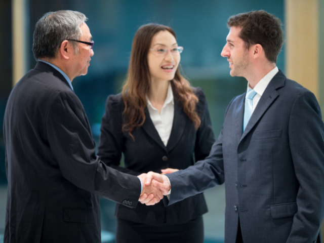Two businessmen shaking hands with a certified interpreter facilitating their conversationpng